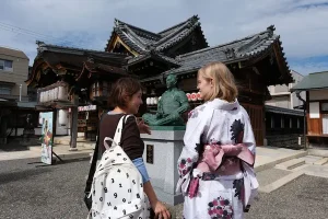 Visitors in traditional kimono listening to a local guide explain the history of Toyotomi Hideyoshi at a shrine in Nagahama